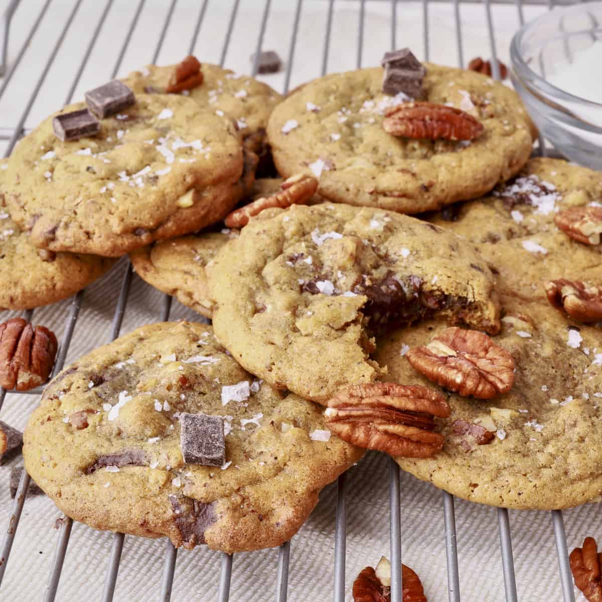 Chocolate Chunk Pecan Cookies piles on a wire rack, sprinkles with salt and pecans.