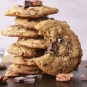 A stack of chocolate chunk pecan cookies with one bitten cookie resting up against the stack.