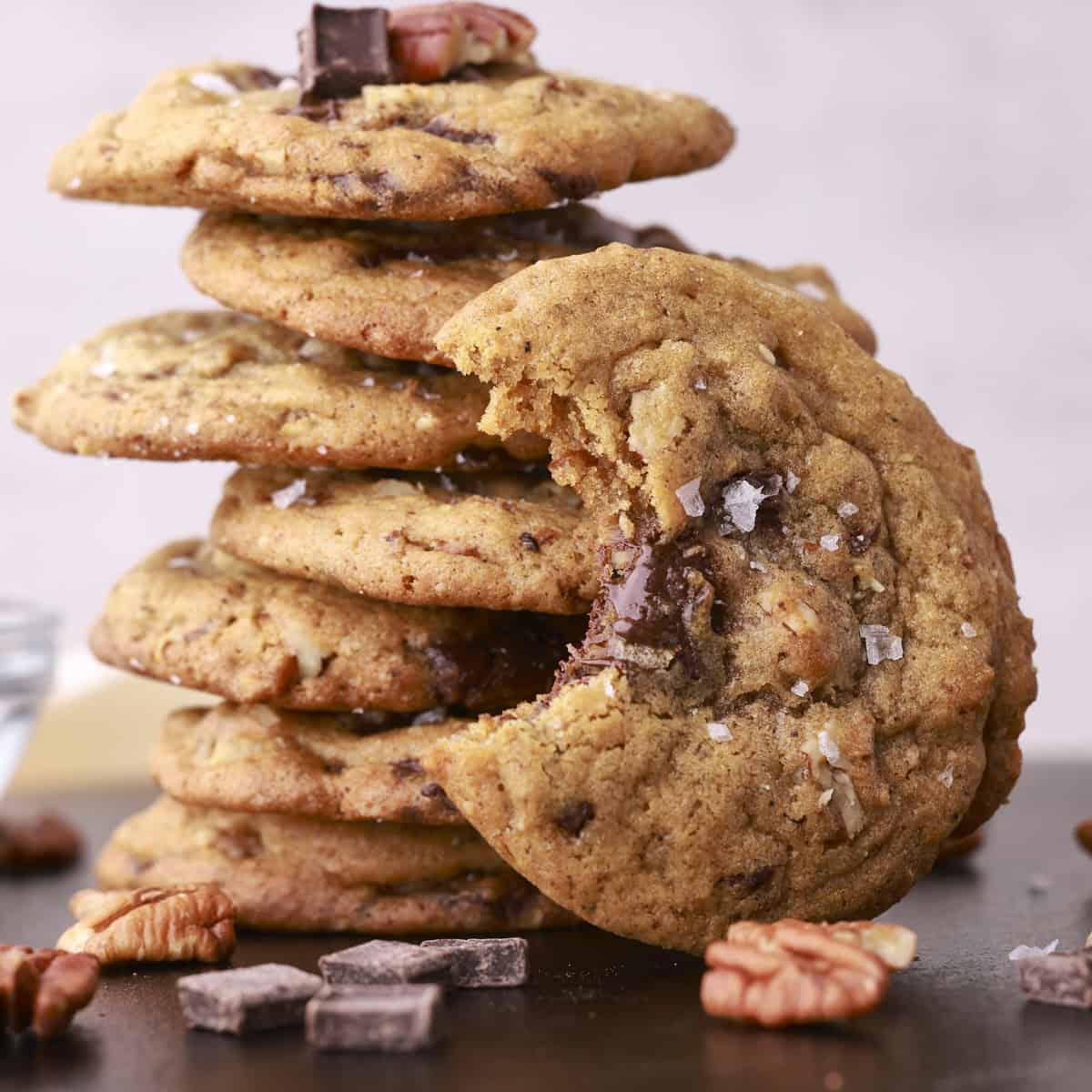 A stack of chocolate chunk pecan cookies with one bitten cookie resting up against the stack.