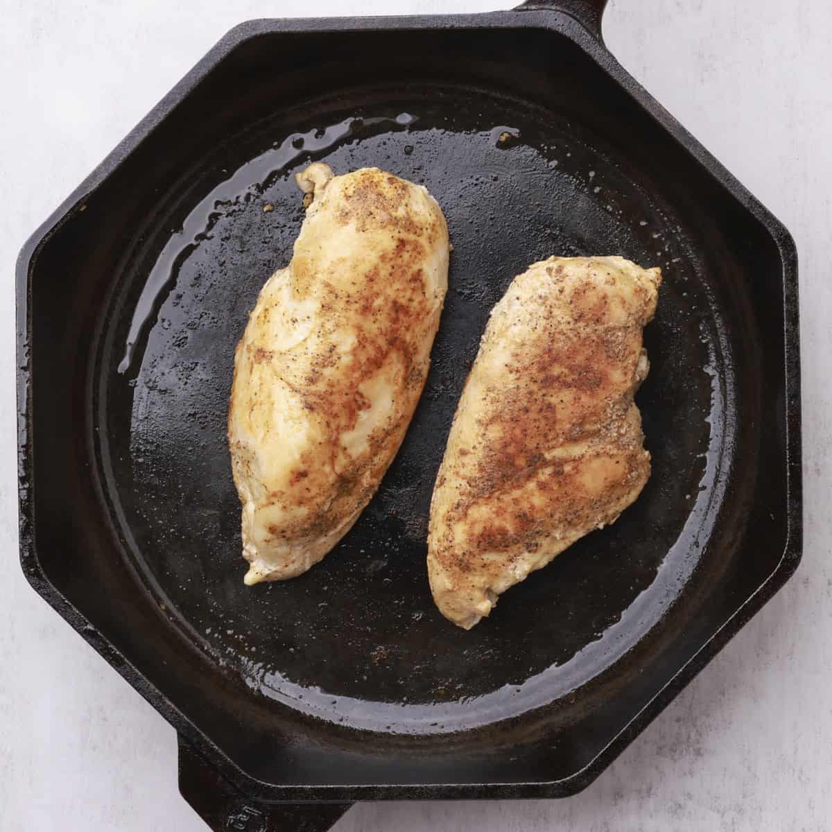 A skillet with two cooked chicken breasts in it.