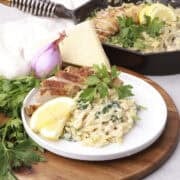 A plate of Lemon Chicken Orzo Pasta displayed with greens and the skillet of pasta in the background.