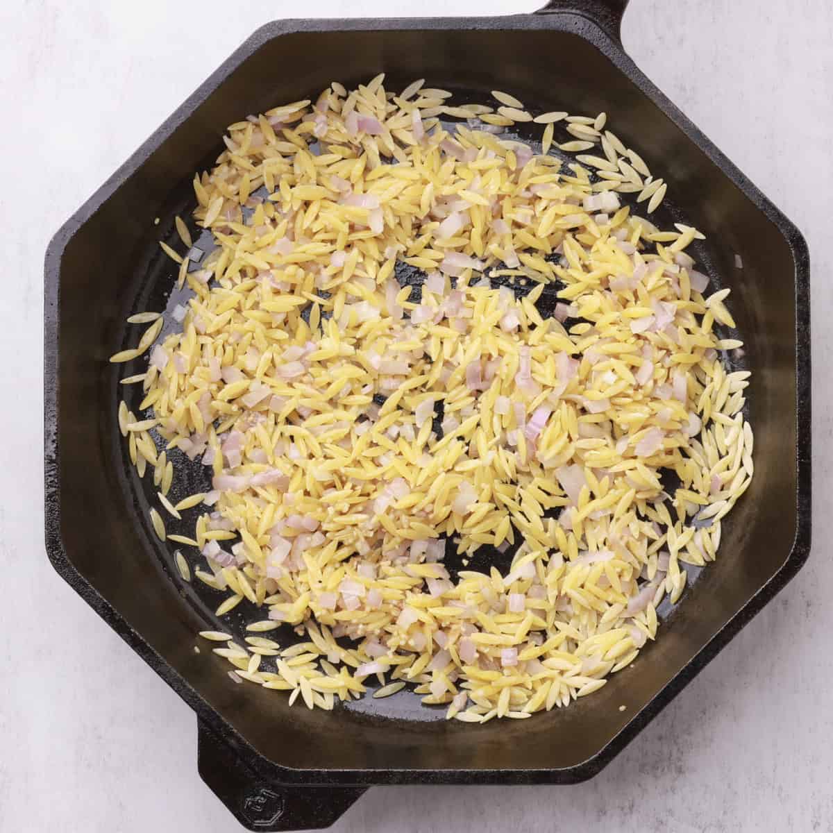 A skillet with the sauteed onions, garlic and orzo in it.