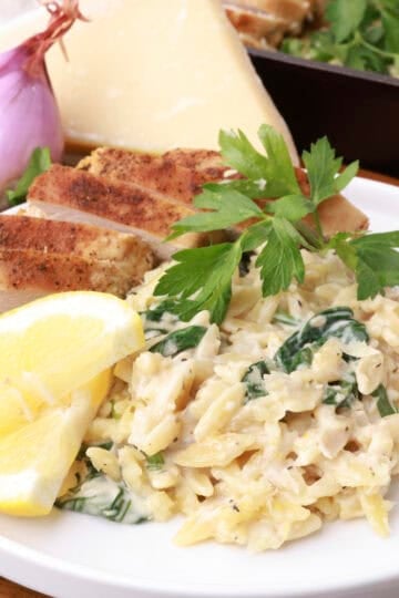 A white plate of Lemon Chicken Orzo Pasta topped with parsley and lemon wedges.