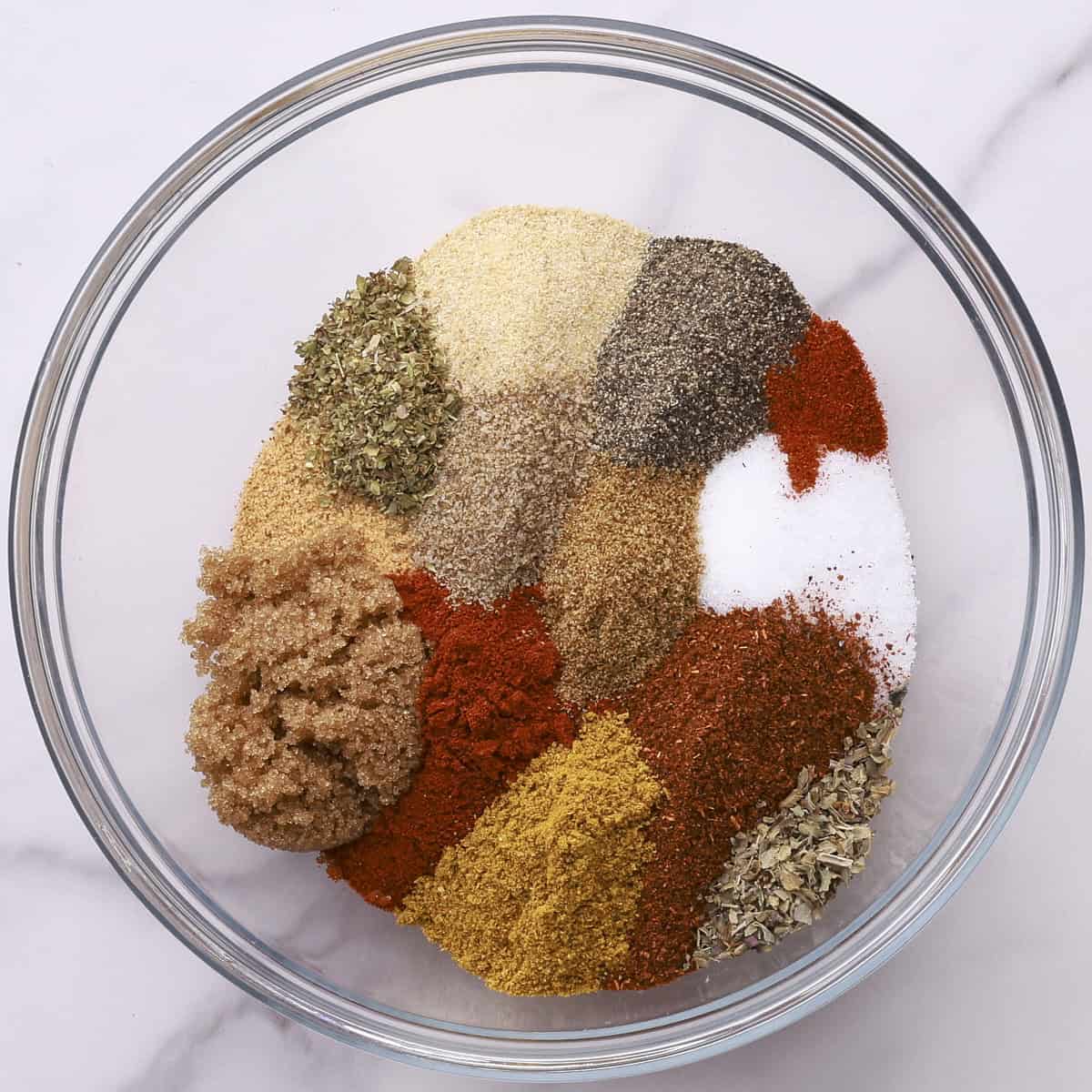 A glass bowl with all the spices poured in but not mixed together.