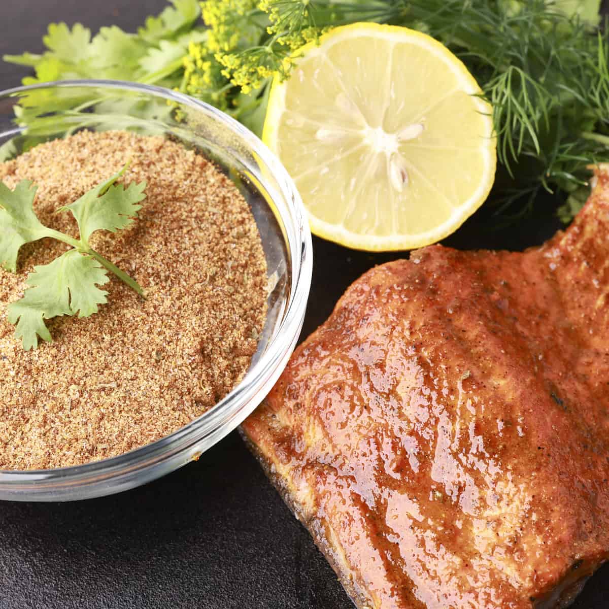A bowl of salmon spice displayed beside a cooked salmon filet with a half of lemon and greens.