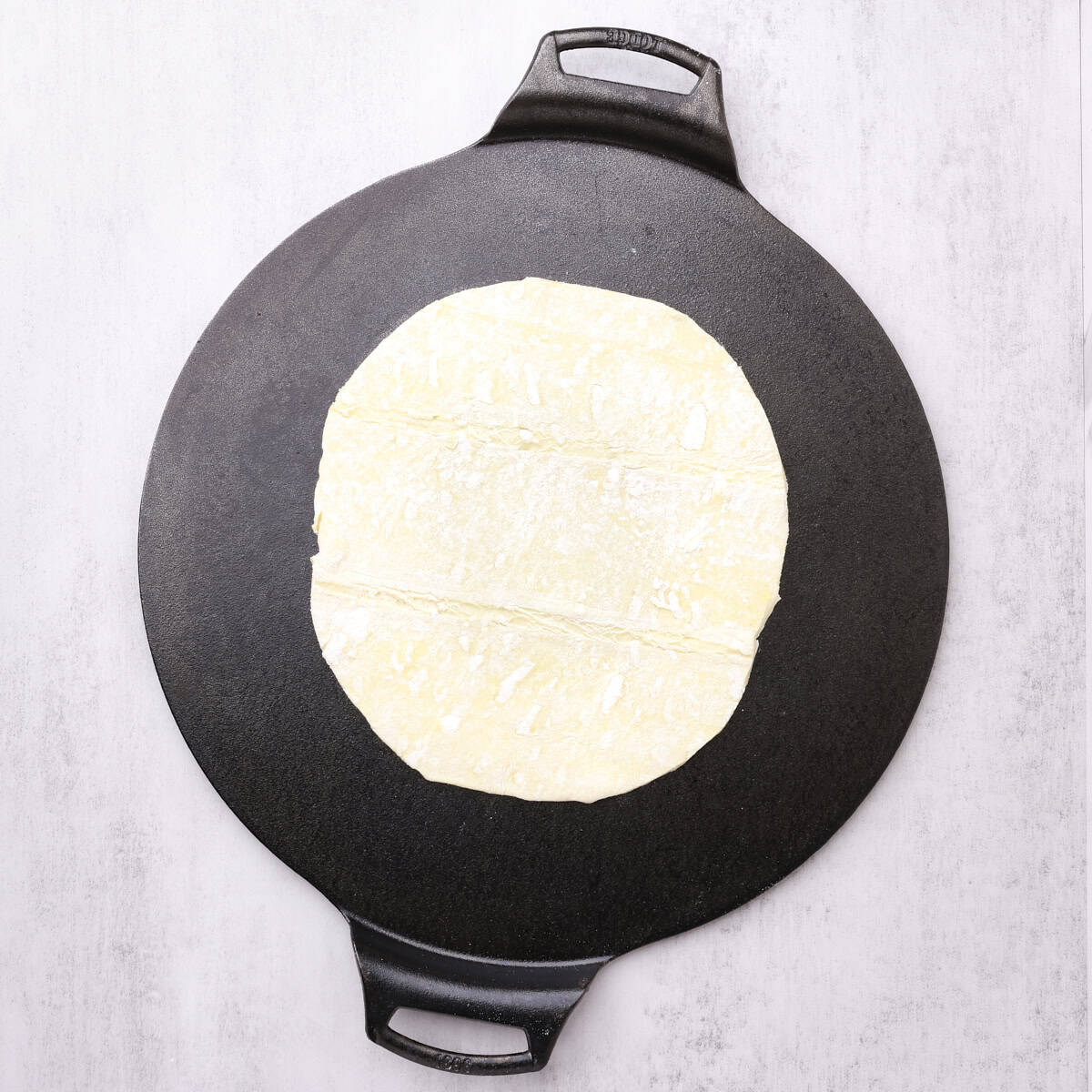 A cast iron pan with a sheet of round(ish) puff pastry laid out on it.