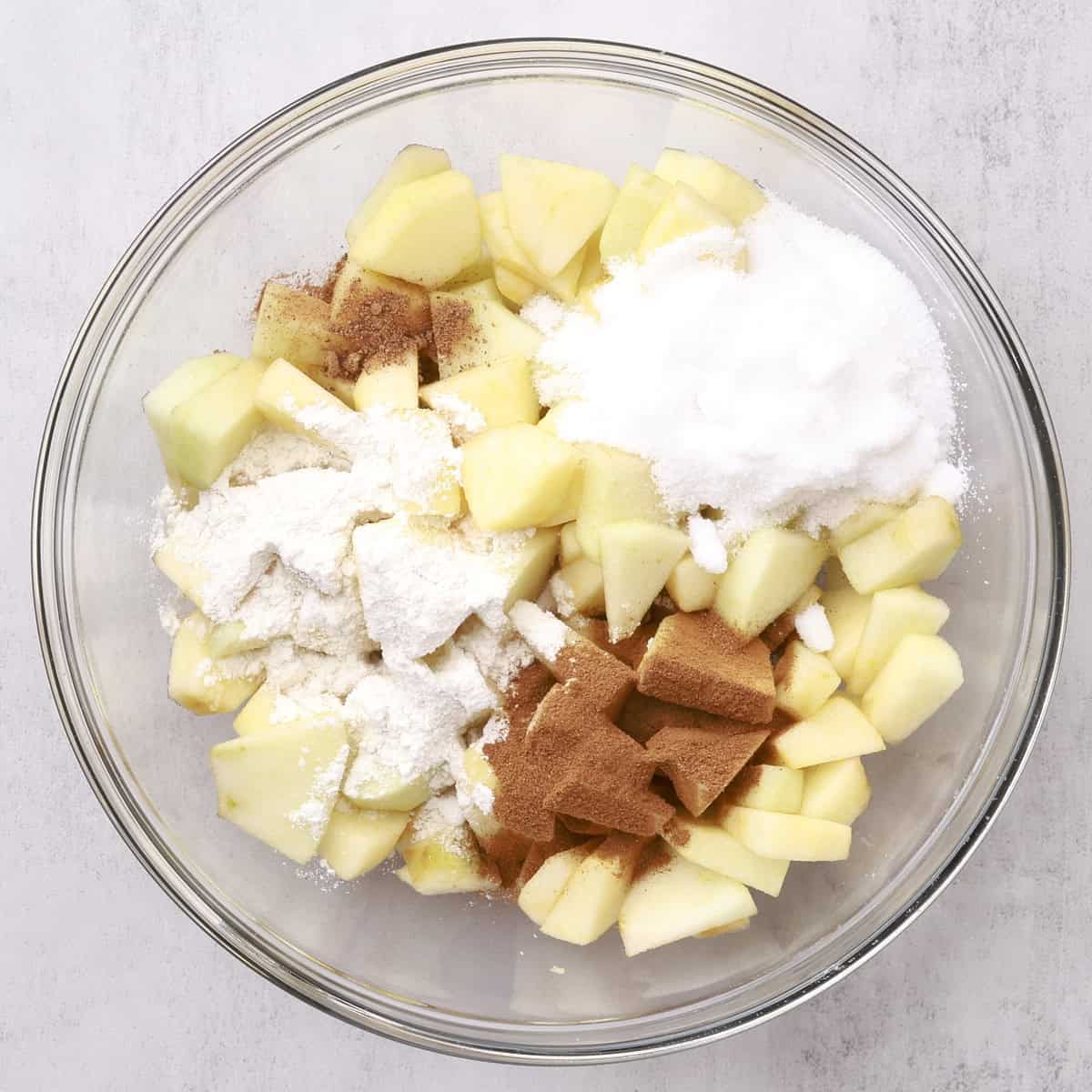 A glass bowl full of sliced apples with the spices and sugar on top.