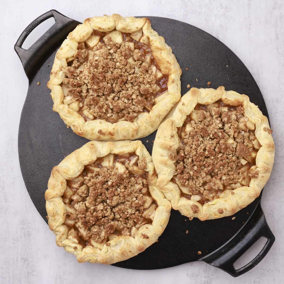 Three apple pies baked on a cast iron sheet to golden brown.