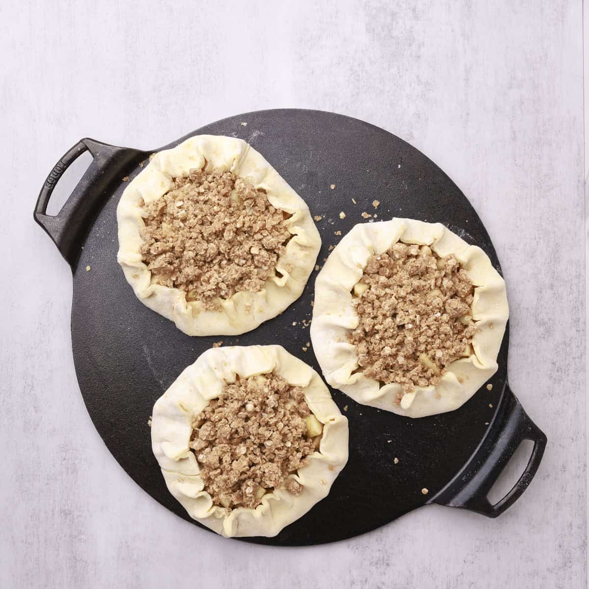 Three apple pies on a cast iron sheet, formed and ready to bake.