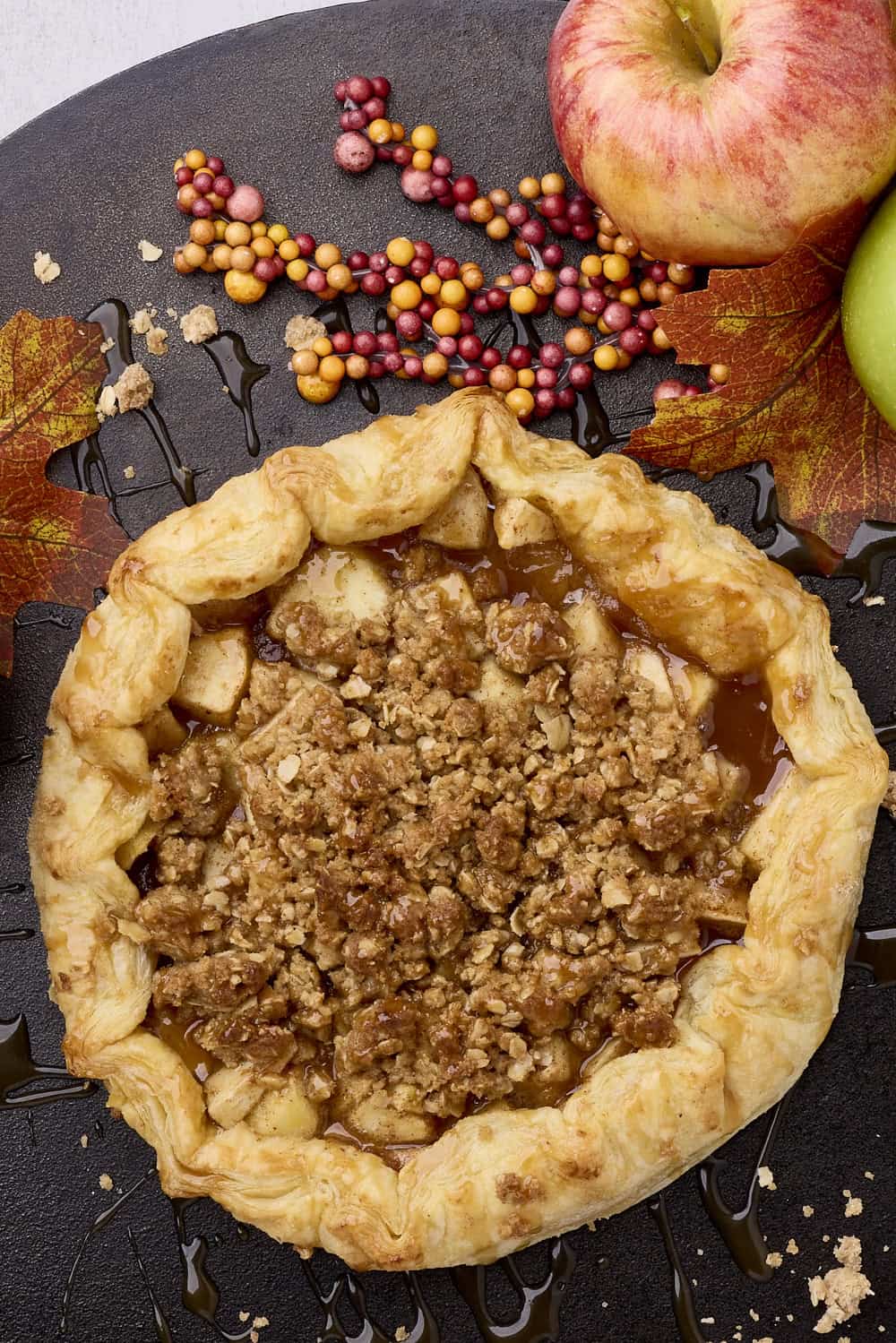 Freshly baked apple pie with crumb topping and seasonal fall decorations.