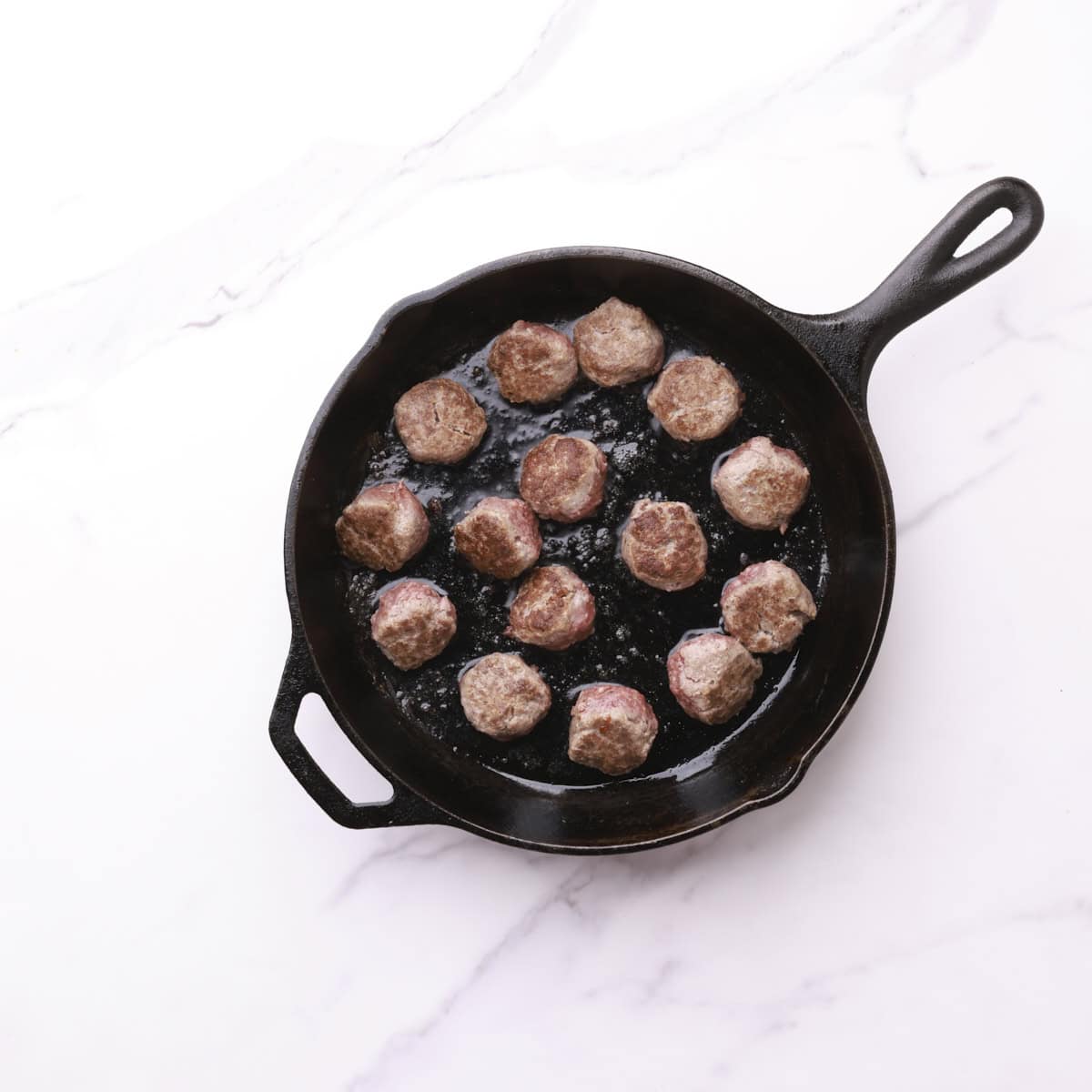 A skillet with browned meatballs in it.
