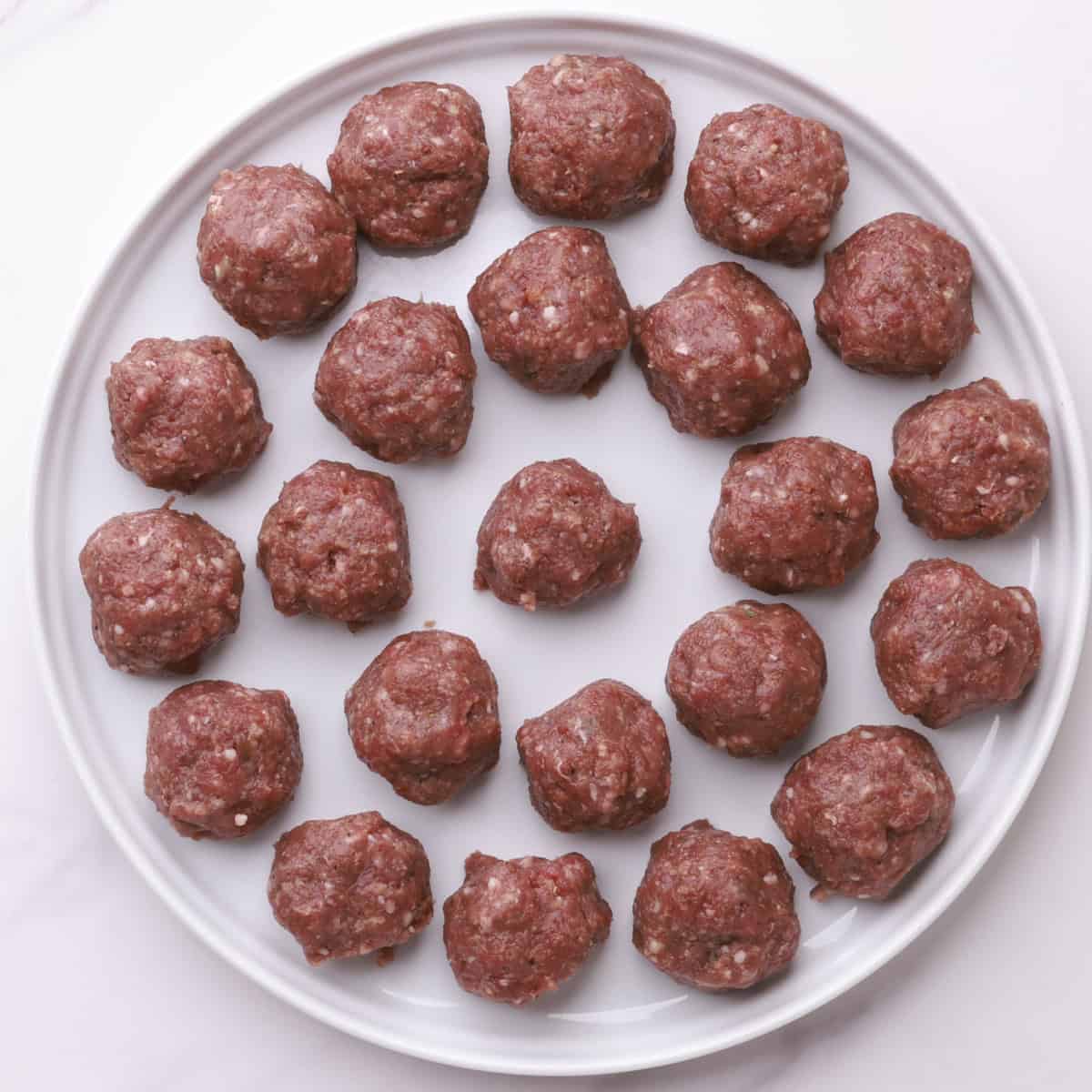 A plate filled with uncooked meatballs.