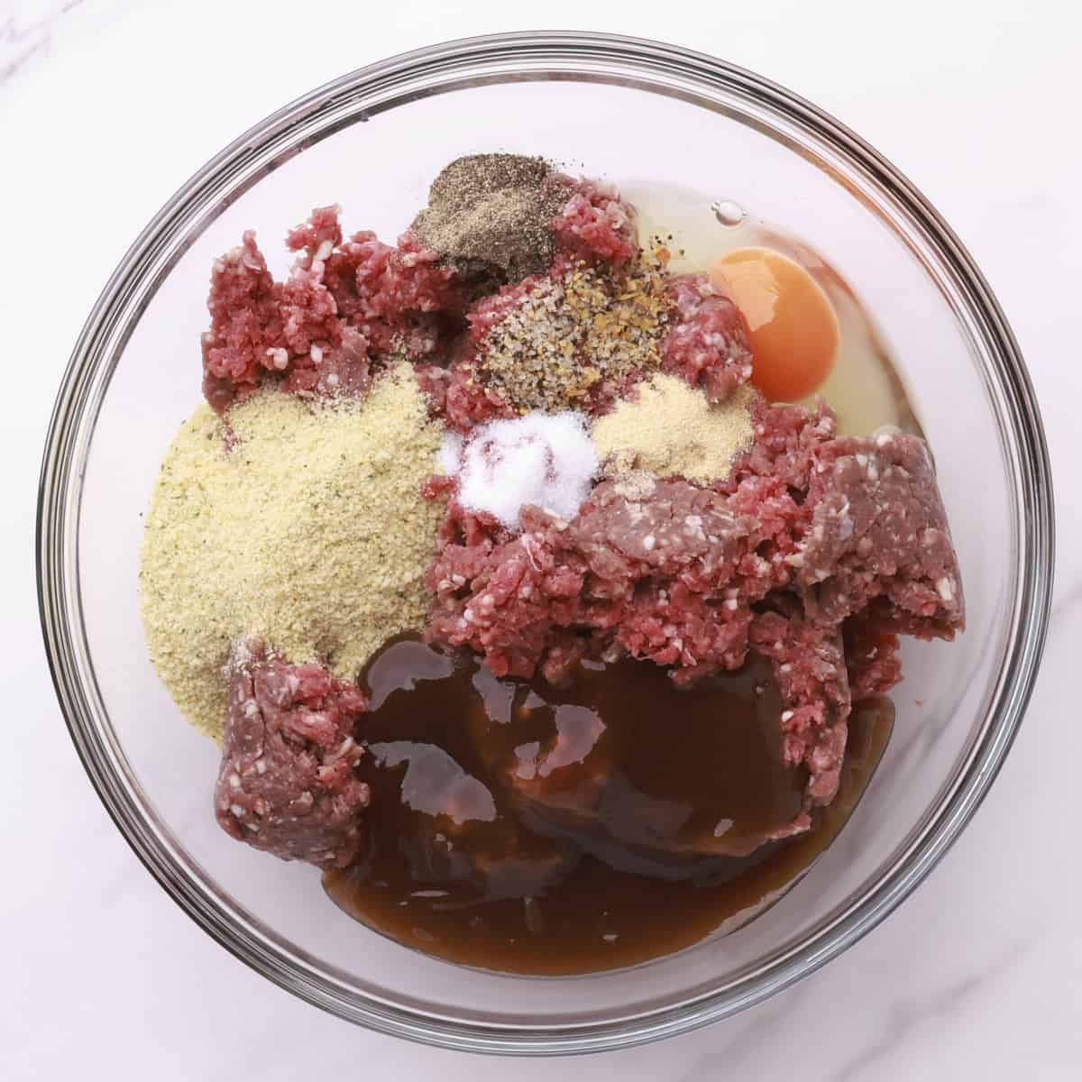A glass bowl filled with all the meatball ingredients.