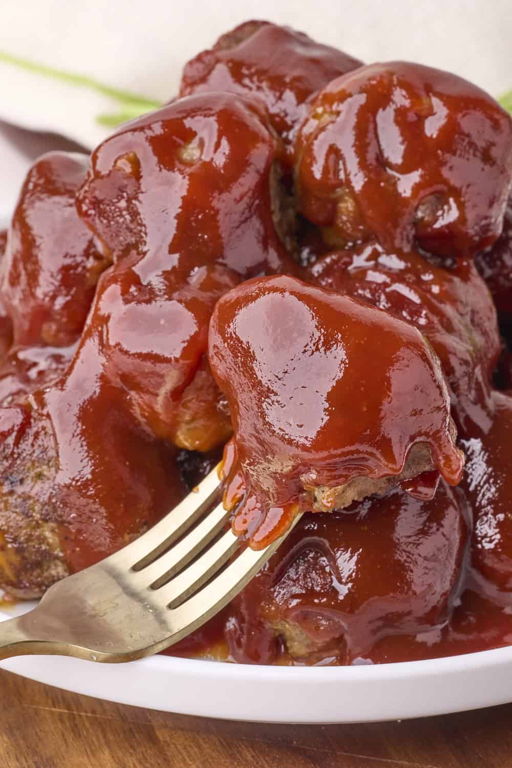 A plate of stacked meatballs with one on a fork.