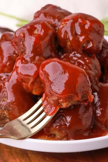 A plate of Crockpot BBQ Meatballs stacked on it, one on a fork positioned at the front.
