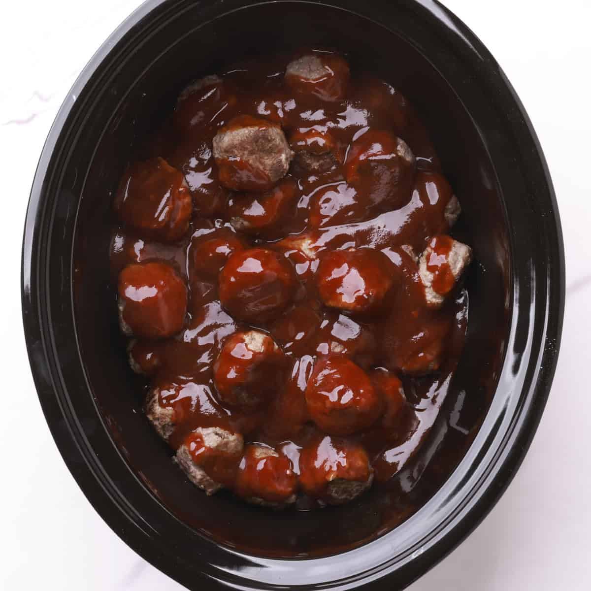 A crockpot with the meatballs in it covered in bbq sauce.
