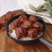 A skillet with rice topped with meatballs, displayed on a wooden board.