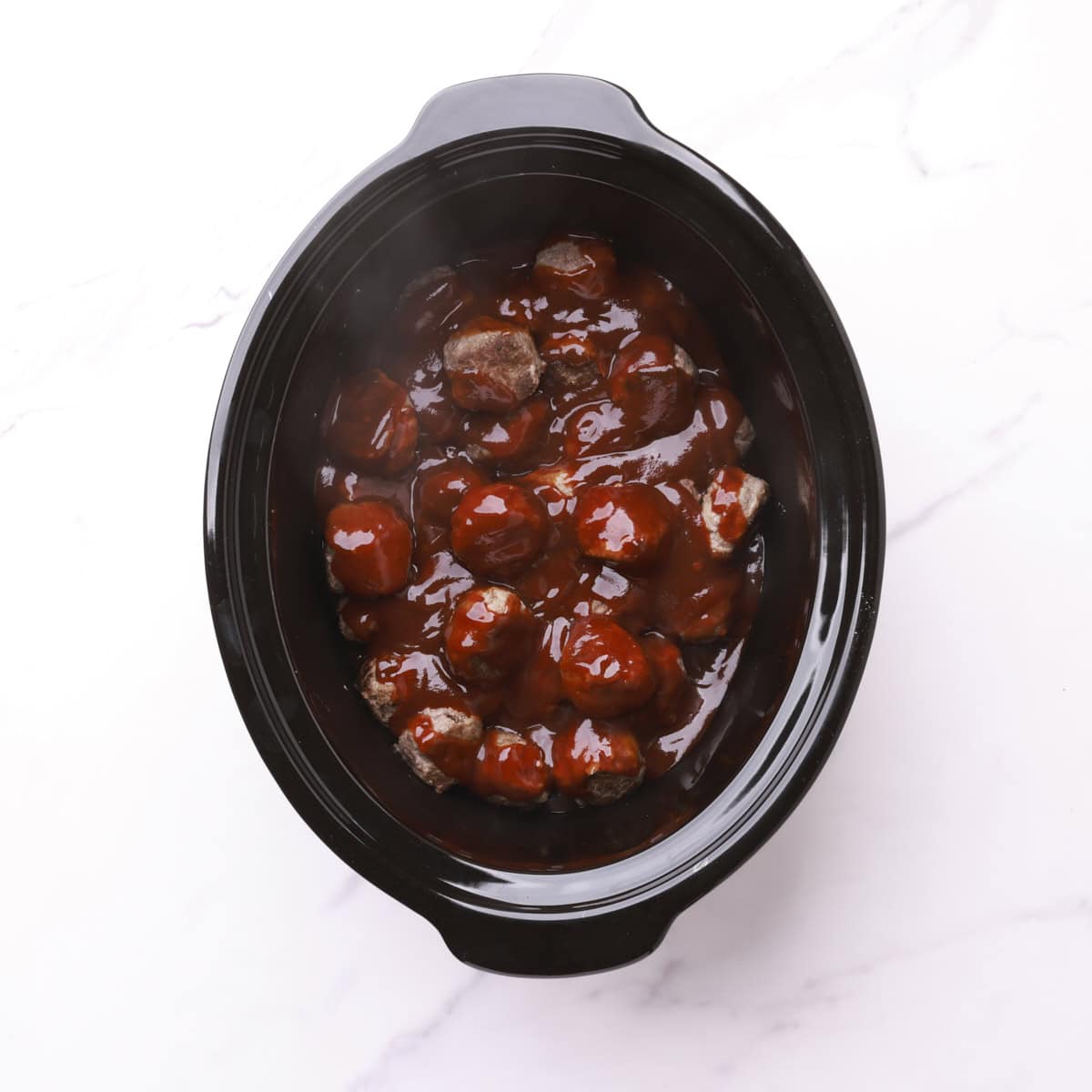 A crockpot with the cooked bbq meatballs in it.