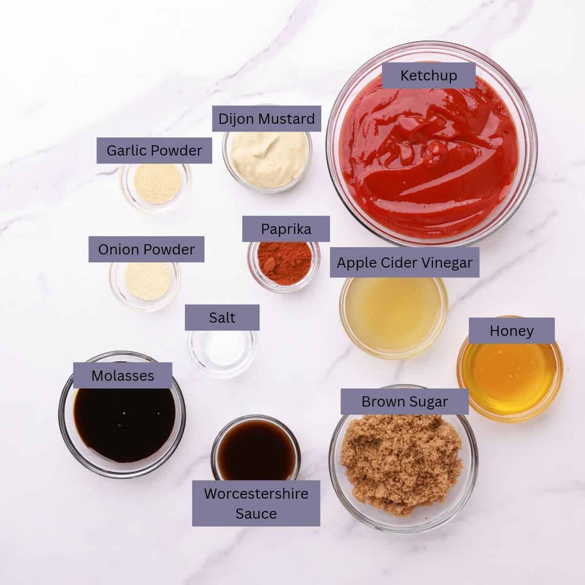 A visual display of the ingredients needed for the Homemade BBQ Sauce - ketchup, Dijon mustard, garlic powder, onion powder, paprika, salt, Worcestershire sauce, molasses, brown sugar, apple cider vinegar and honey - each displayed in their own bowl.