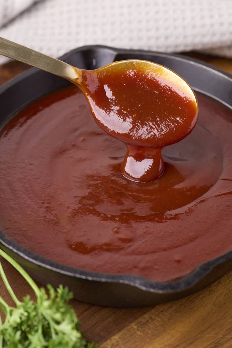 Homemade BBQ Sauce in a skillet with sauce drizzling off a spoon above.