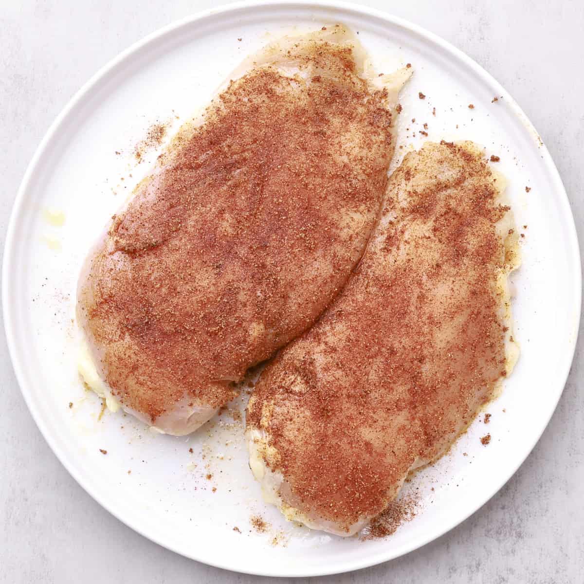 A white plate with two seasoned chicken breasts on it.