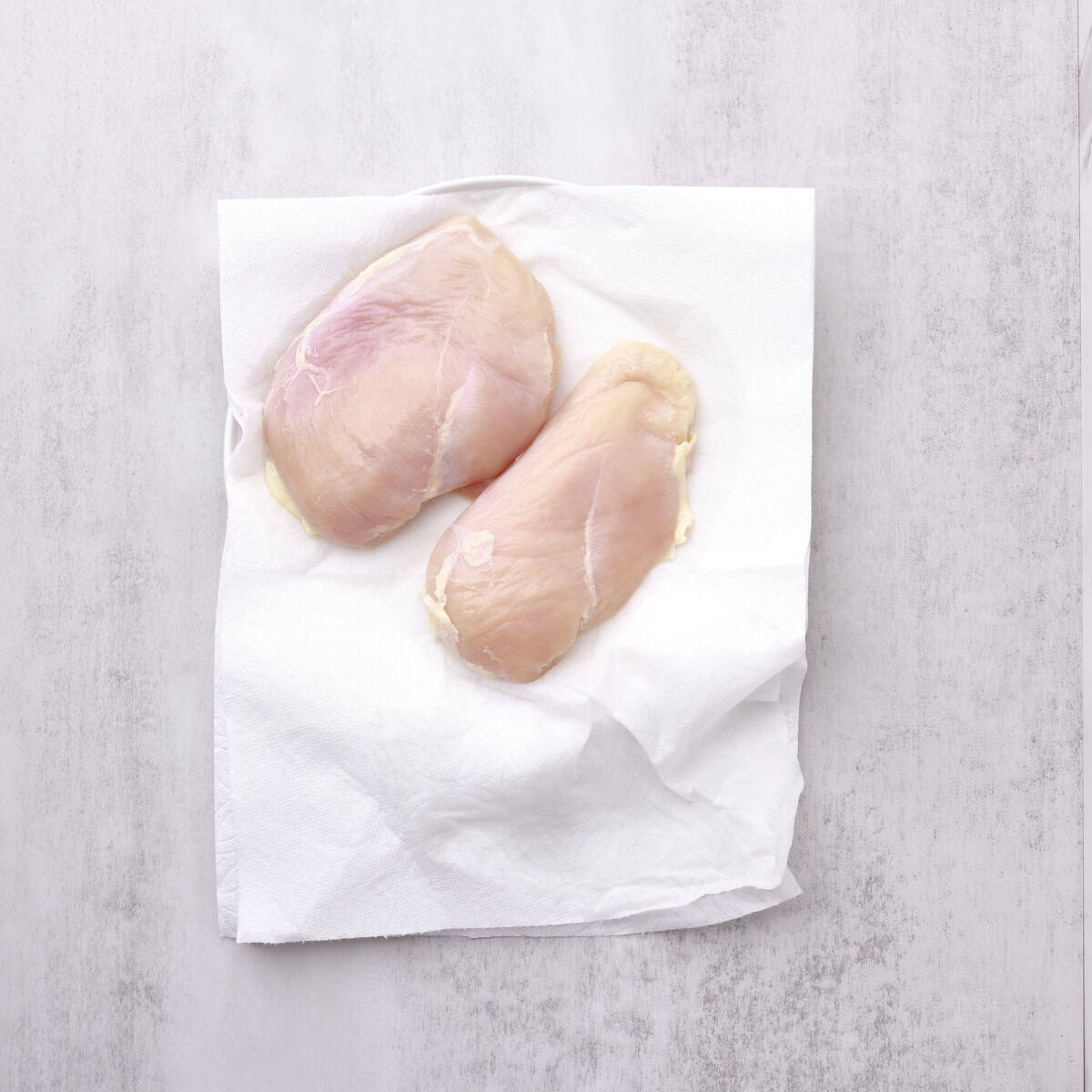 Two chicken breasts sitting on a plate covered with paper towel.