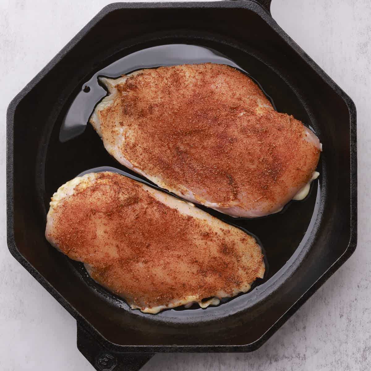 A skillet with the two seasoned, uncooked chicken breasts in it.
