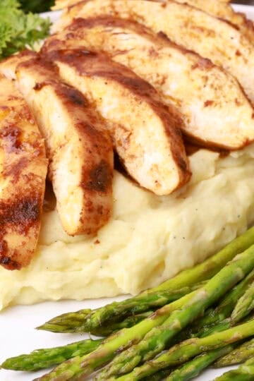 The cast iron skillet chicken breast sliced and laid atop mashed potatoes with a side of asparagus.