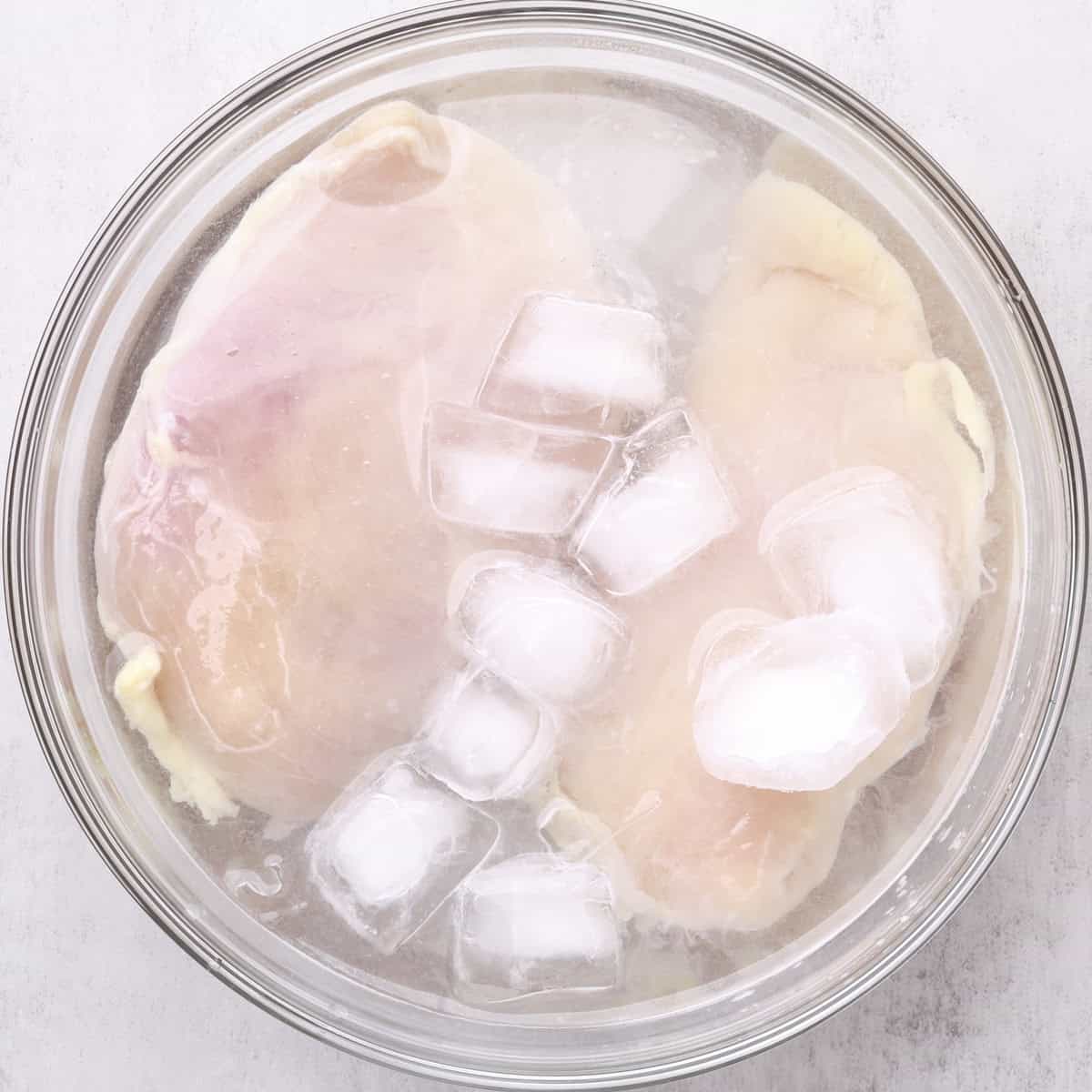A glass bowl filled with ice salt water covering the chicken breasts.